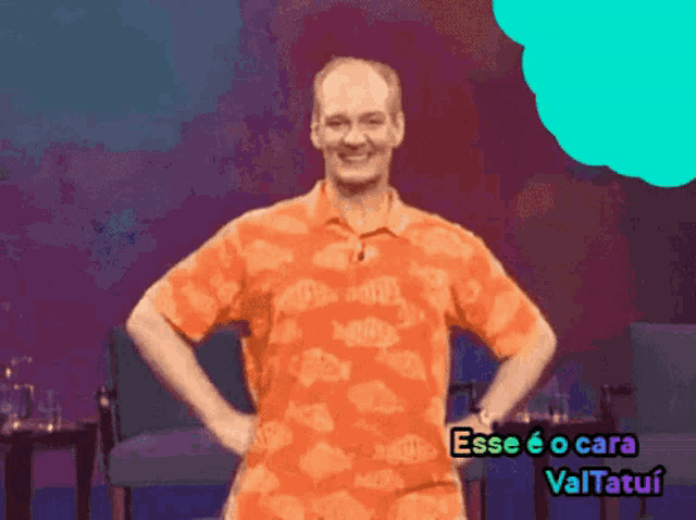 a man in an orange shirt stands with his hands on his hips and says esse eo cara