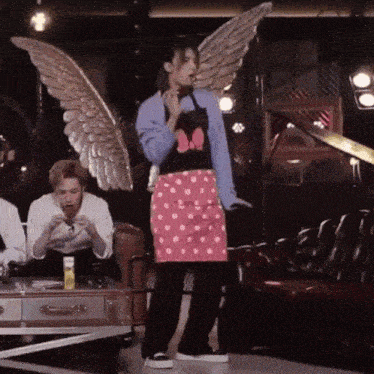 a woman wearing a minnie mouse apron and wings is standing in front of a group of people .
