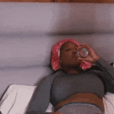a woman laying on a bed drinking water from a glass