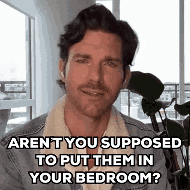 a man in a denim jacket is talking on a video call while wearing ear buds and a plant .