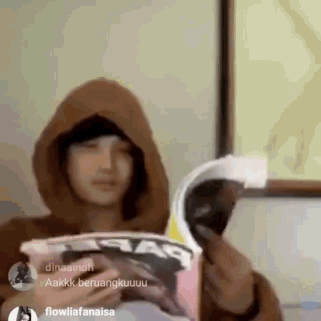 a woman in a hoodie is reading a magazine .