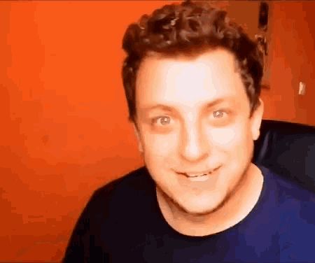 a man with curly hair wearing a blue shirt is smiling