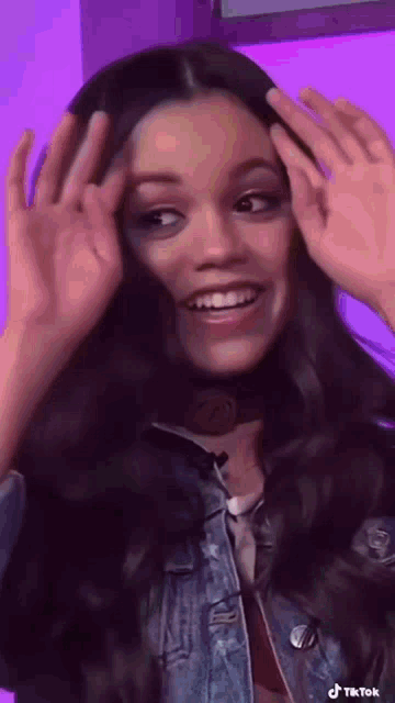 a woman in a denim jacket is smiling and making a funny face with her hands .