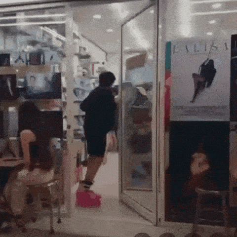 a man is standing in the doorway of a store with a woman sitting on a stool .