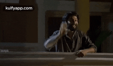 a man with a beard is waving his hand in front of a screen that says kulfyapp.com
