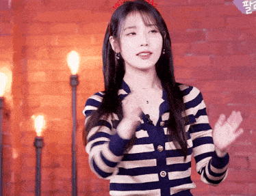 a woman wearing a striped sweater stands in front of a brick wall and candles