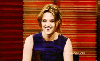 a woman in a blue dress is smiling in front of a wall that says wednesday on it