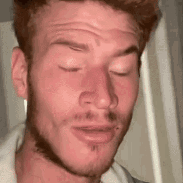 a close up of a man 's face with his eyes closed and a beard .