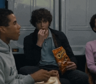 a man is eating a bag of cheetos while sitting next to another man