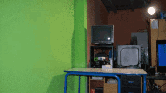 a green wall behind a desk with a tv on top