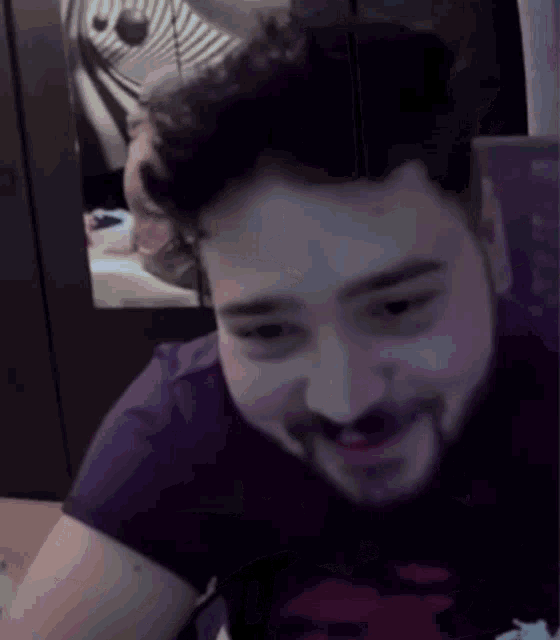 a man with a beard wearing a purple shirt is smiling and looking at the camera