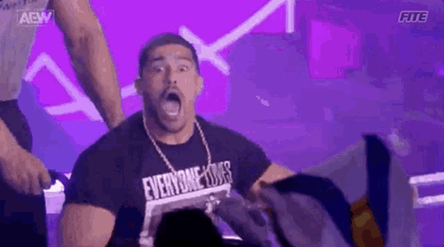 a man wearing a t-shirt that says `` everyone does '' is standing on a stage .