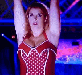 a woman in a red corset with white polka dots holds her arms up in the air