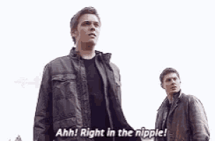 two men are standing next to each other and one of them is holding his chest and saying `` right in the nipple '' .