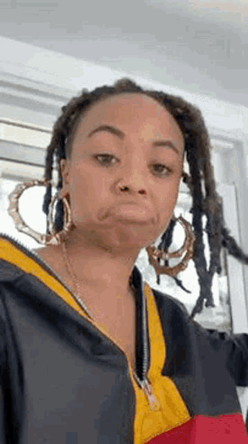 a woman with dreadlocks is wearing hoop earrings and making a funny face .