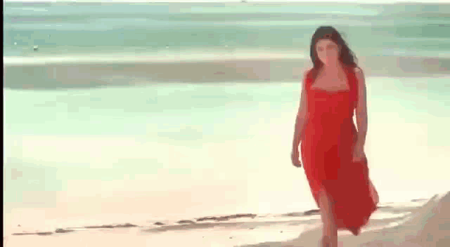 a woman in a red dress is walking along a beach .