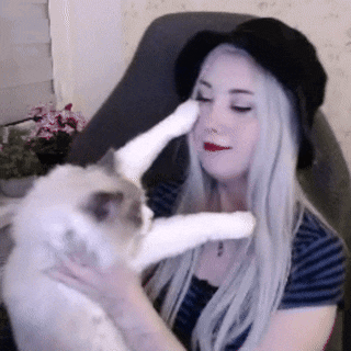 a woman wearing a black hat holds a cat 's paw to her face