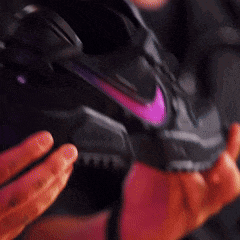 a person is holding a black nike shoe with a purple swoosh