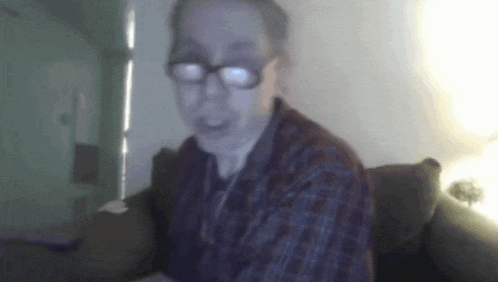 a man wearing glasses is sitting on a couch in front of a computer screen .