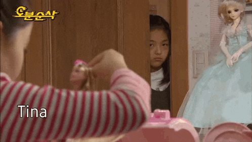 a little girl is looking at herself in the mirror while a doll is standing next to her .