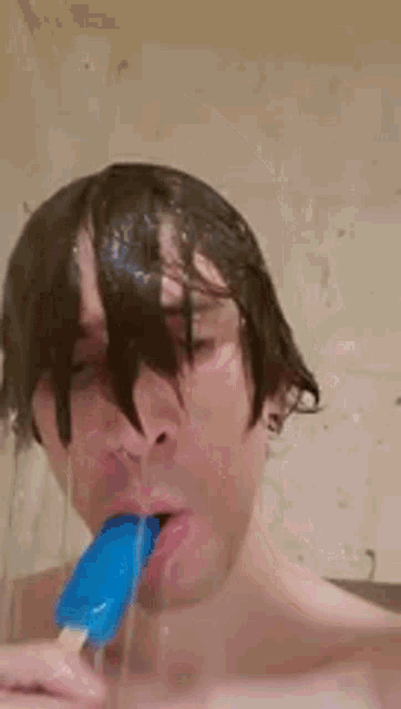 a man without a shirt is eating a blue popsicle in a shower .