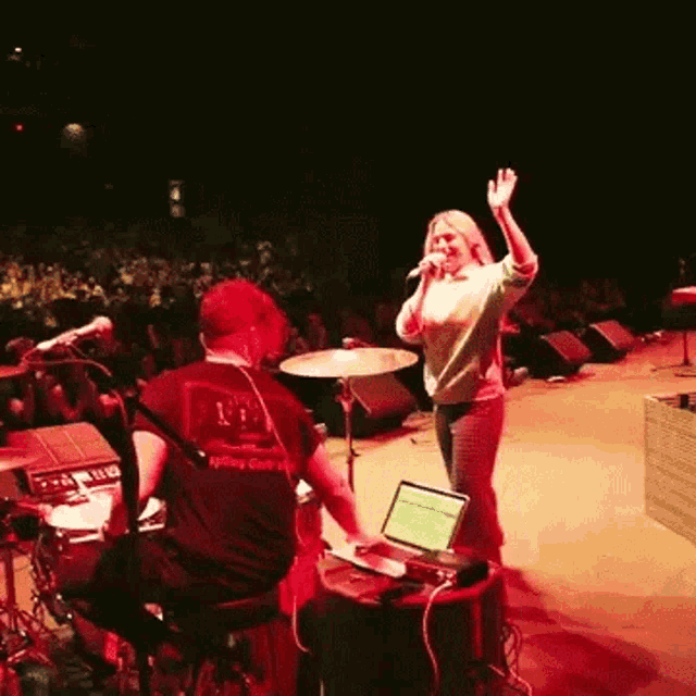 a woman singing on stage with a man playing drums behind her