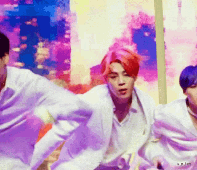 a group of men are dancing in front of a colorful background . one of the men has red hair .