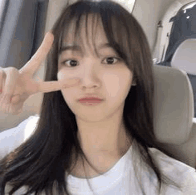 a young woman is sitting in a car making a peace sign with her hand .