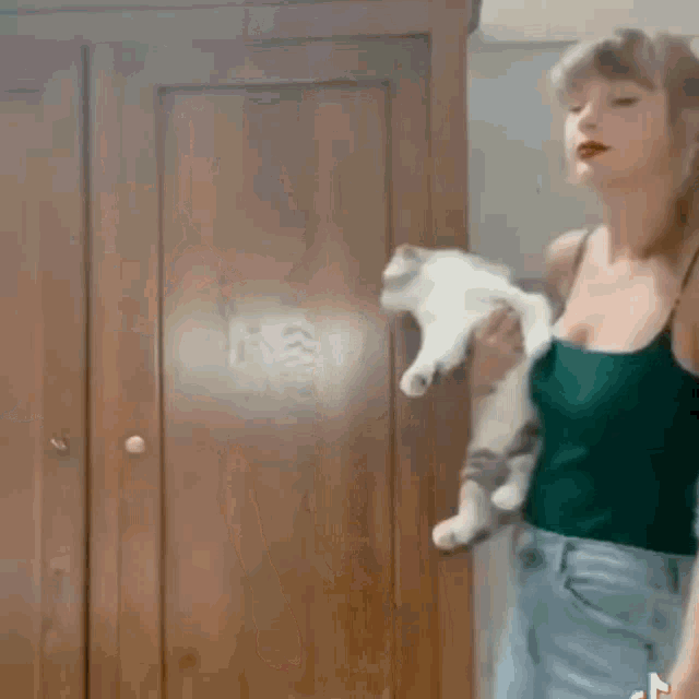a woman in a green tank top and blue jeans is dancing in front of a door .