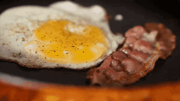 two eggs and bacon are cooking in a frying pan