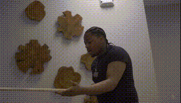 a man is holding a wooden stick in front of a wall with wooden sculptures .