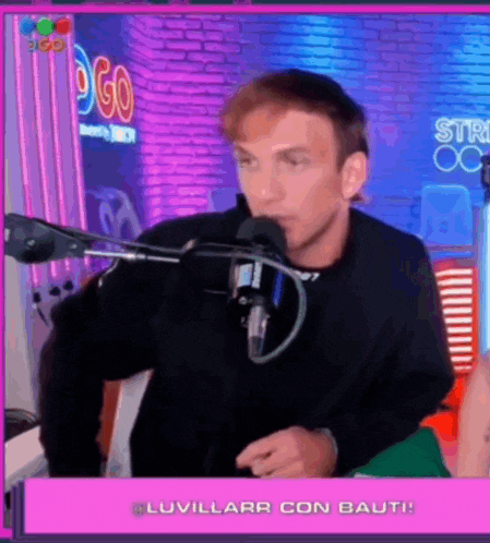 a man is talking into a microphone while sitting in front of a pink screen .