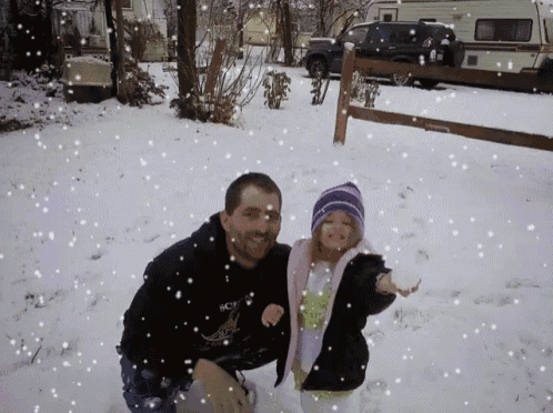 a man and a little girl are playing in the snow and the little girl is wearing a pink jacket