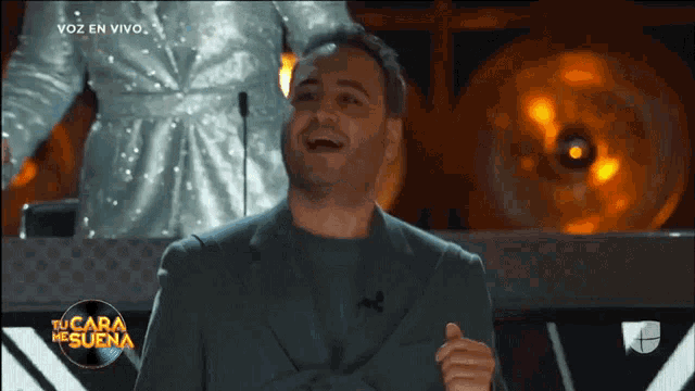 a man laughs in front of a tv screen that says voz en vivo