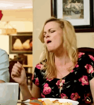 a woman wearing a floral shirt is sitting at a table with a plate of food