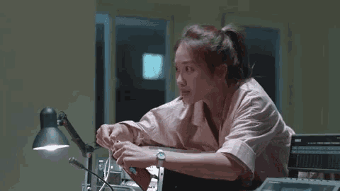 a woman in a pink robe is sitting at a desk in a room with a lamp .