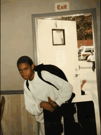 a boy with a backpack stands in front of an exit sign