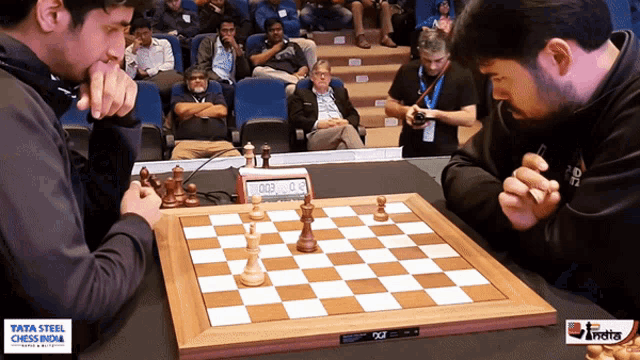 two men are playing chess in front of a tata steel chess india sign