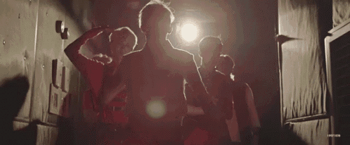 a group of people are standing next to each other in a dark room under a light .