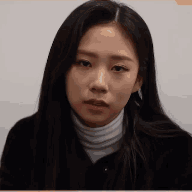 a woman with long black hair is wearing a white turtleneck and black jacket .