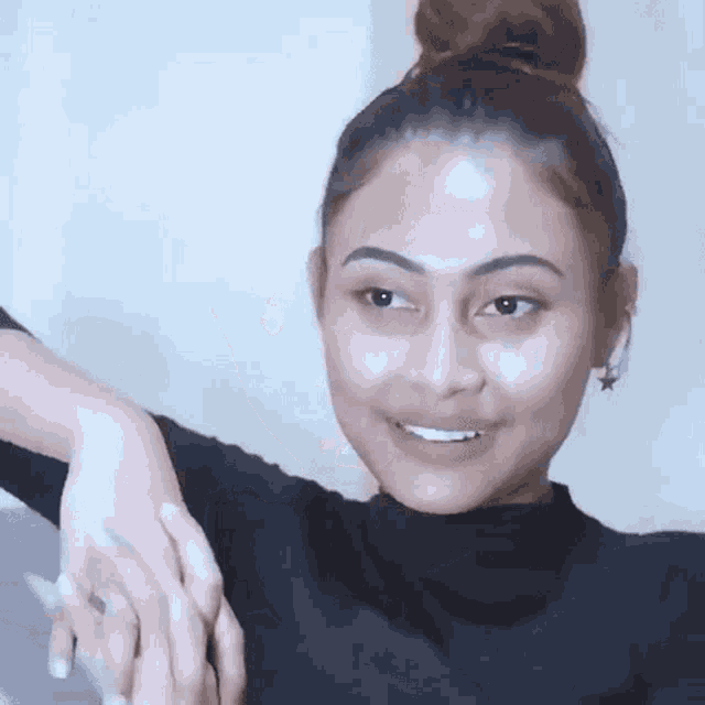 a woman with her hair in a bun is smiling and applying lotion to her wrist .