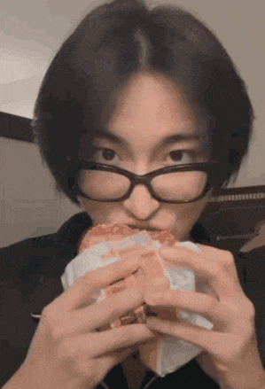 a person wearing glasses is eating a hamburger
