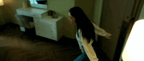 a woman with long black hair is walking in a room
