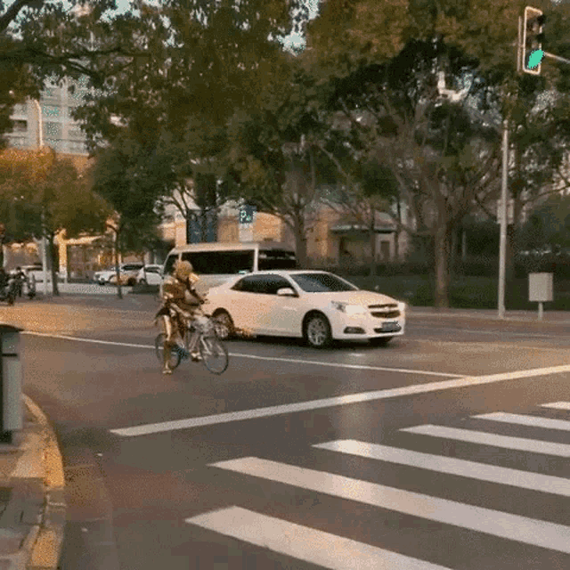 a man is riding a bike in front of a white car at an intersection .