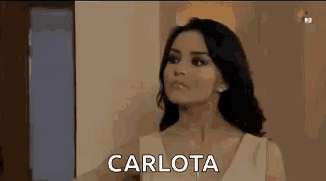 a woman in a white dress is standing in front of a door and says carlota .