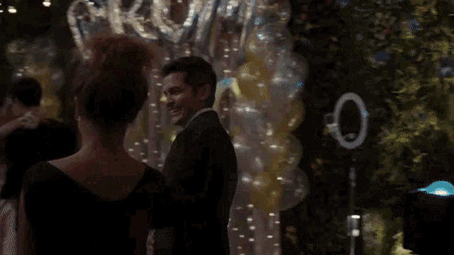 a man and a woman are dancing at a prom with balloons and lights in the background .