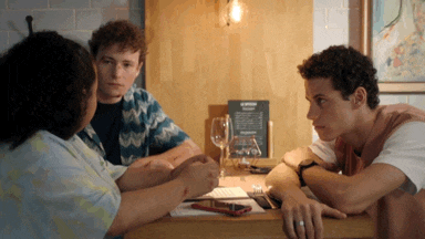 a group of people sit at a table with a menu on the wall behind them