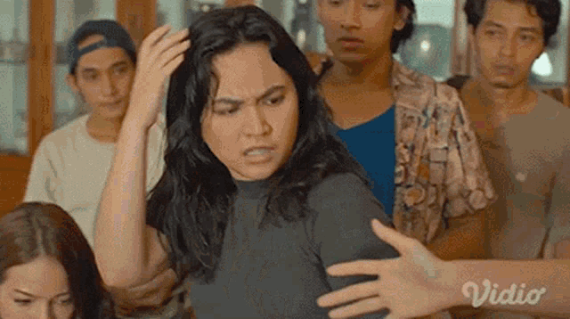 a woman is standing in front of a group of people and holding her head .