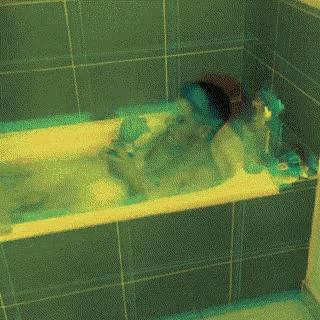 a person is taking a bath in a bathtub with green tile walls