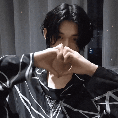 a man with long black hair is making a heart with his hands
